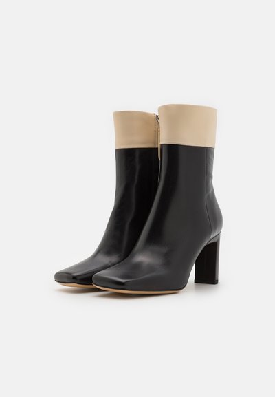 Black leather ankle boots with a square toe, contrasting beige upper, and a block heel. Features a side zipper for easy wear.