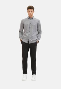 Chemise à carreaux noire et blanche, assortie à un pantalon noir et des baskets blanches. La chemise a des manches longues et un col.