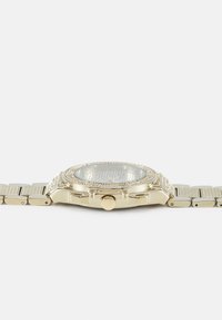 Gullfarget klokke med teksturert bezel, klar klokkeplate og en metallarmbånd med vekslende glatte og teksturerte lenker.