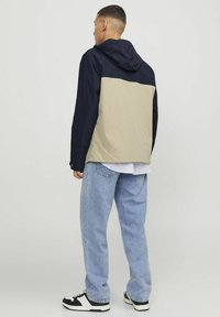 Jachetă color-block cu partea superioară bleumarin și jumătatea inferioară bej, cu glugă și o textură ușoară și netedă. Purtați-o peste o cămașă în dungi.