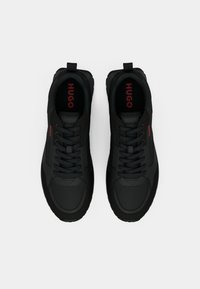 Black low-top sneakers with laces, featuring "HUGO" branding in red on the insoles and sides, displayed on a white background.