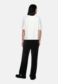 White short-sleeve top with a straight cut, paired with black wide-leg corduroy pants featuring subtle vertical stripes and a logo detail.