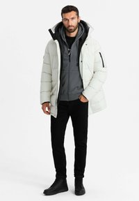 Giacca puffa bianca con colletto alto sopra un felpa grigia, abbinata a jeans neri e stivali neri con lacci. Tessuti testurizzati, tasche con cerniera.