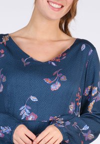 Bluse mit blauem Blumenmuster, V-Ausschnitt, langen Ärmel mit gerafften Manschetten und einem strukturierten Stoff mit kleinen Punkten.