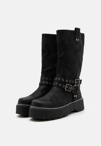 Black suede knee-high boots with a thick platform sole, silver hardware accents, and decorative buckle straps. Textured finish, rugged design.