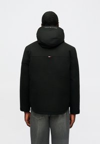 Čierna kapucňová bunda s hladkým povrchom, ktorá má logo na krku a malý trojfarebný akcent na chrbte pri golieri.