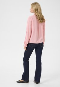 Light pink long-sleeve blouse with gathered cuffs, paired with dark blue flared jeans. Black ballet flats with a bow accent. Minimalist design.
