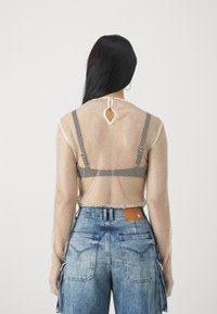 Kvinne med langt mørkt hår iført en hvit nett langermet topp over en svart BH og høytlivede blå denimjeans, vist fra bak.