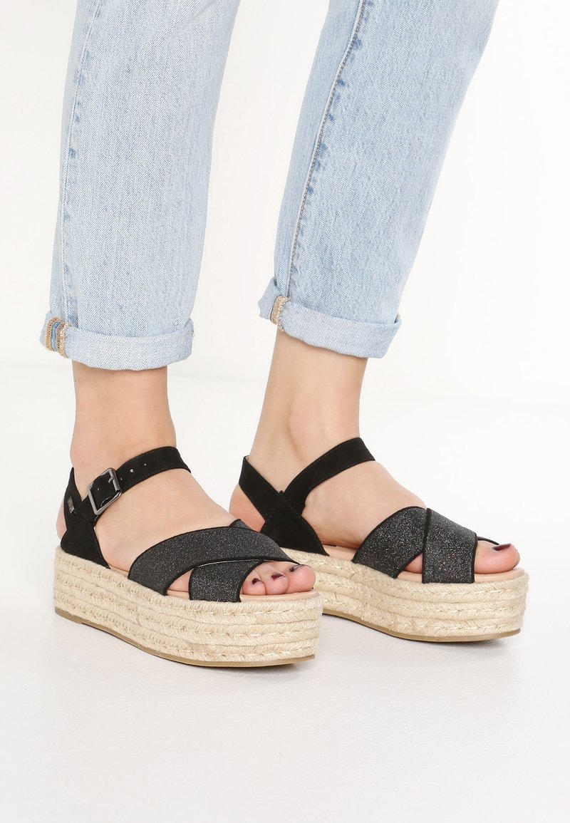 Czarne sandały espadryle z teksturowaną cholewką, plecioną platformą z juty oraz regulowanym paskiem na kostkę; zaprojektowane w stylu z krzyżującymi się paskami.