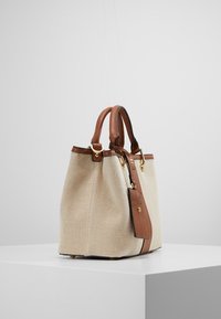 Béžová taška z plátna s herringbone vzorem, hnědými koženými akcenty, dvojitými uchy a odnímatelným popruhem. Zlaté kovové prvky a texturovaný povrch.