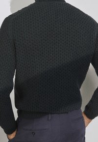 Ciemnozielony dziany sweter z fakturowanym wzorem, ściągaczami na mankietach i dolnym brzegu oraz klasycznym kołnierzem. Widok pokazuje tył i rękawy.