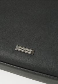 Borsa a tracolla in ecopelle nera con una texture sottile e una placca logo metallica che riporta la scritta "ALDO". Design semplice e rettangolare.