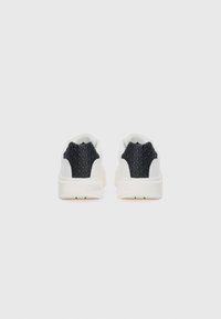 Adidași albi cu accente texturate negre la călcâi. Corp din piele netedă, formă rotunjită și talpă groasă de culoare crem. Design minimalist.
