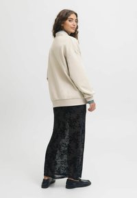 Oversized beige sweatshirt, black sheer floral skirt, textured fabric, relaxed fit, and black shoes. Back view with neutral background.