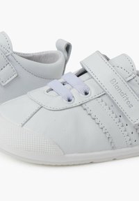Svetle šedé kožené sneakers s texturovanou špičkou, tkanými detaily a páskem na suchý zip pro nastavitelné uchycení. Součástí jsou bílé tkaničky.