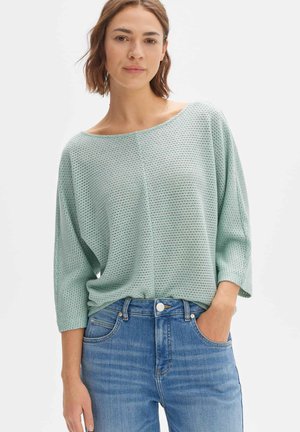 Helle mintgrüne, locker sitzende Strickoberteil mit weitem Bootsausschnitt und Dreiviertelärmeln, kombiniert mit blauen Jeans.