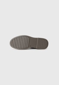 Suela de zapato de goma marrón con textura acanalada horizontal y vertical, punta redondeada y un ligero tacón. Presenta una superficie lisa y plana.