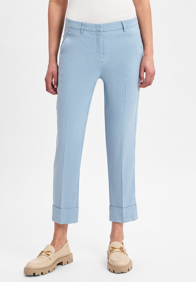 Lichtblauwe op maat gemaakte broek met een gladde textuur, met een cropped lengte en opgerolde manchetten. G gedragen met beige instappers.