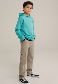 Ljus aqua huvtröja med en framficka, ihopparad med khaki cargo-byxor med sidofickor, och svarta sneakers med vita detaljer.