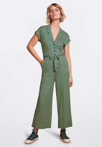 Mono verde con estampado, de manga corta, cintura ceñida y pantalones de pierna ancha. Combinado con zapatillas oscuras y un diseño minimalista.