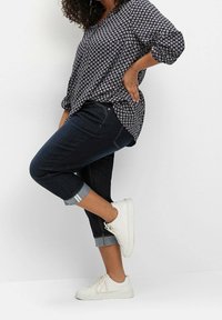 Námořnická blůza s bílým květinovým vzorem, ohrnuté rukávy, tmavé džíny s ohrnutými lemy a bílé tenisky s texturovanou podrážkou.