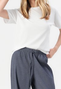 T-shirt blanc en coton à manches courtes, associée à un pantalon ample gris foncé texturé avec une taille élastique.