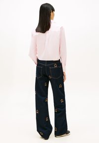 Světle růžová košile s dlouhým rukávem v kombinaci s tmavě modrými širokými džíny s barevnými vyšívanými motivy korun a klasickým pětipokládovým střihem.