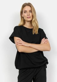 Top corto negro de manga corta en una tela suave con un ajuste relajado, escote redondo y sutil detalle de dobladillo curvado, combinado con pantalones negros.