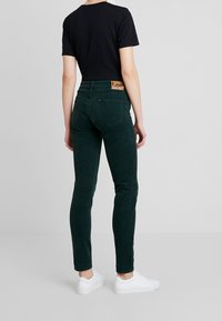 Gröna kordfläckiga byxor har en slim fit, bakfickor och en tan läder etikett i midjan. Matchas med en svart t-shirt och vita sneakers.