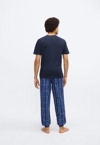 Tricou din bumbac bleumarin cu mâneci scurte, asortat cu pantaloni de pijama în carouri albastre, prevăzuți cu manșete elastice și linii albe contrastante.