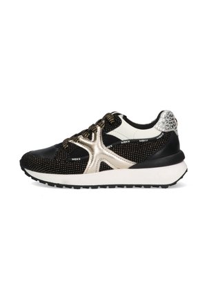 Zwart-witte sneaker met een glanzend gouden accent, een gestructureerde mesh bovenkant, een dikke witte zool en een zwarte rubberen loopzool.