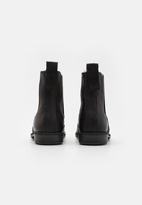 Botas de tobillo de cuero negro con un acabado suave, punta redonda, tiradores en la parte posterior y un tacón bajo apilado.