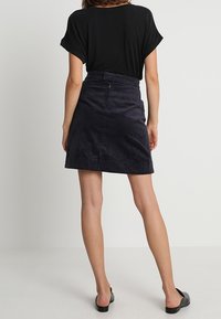 Zwarte T-shirt met omgeslagen mouwen, gecombineerd met een donker corduroy minirok met een achterrits en een gladde textuur. Platte zwarte schoenen.
