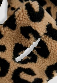 Leopárd mintás szövet, puha textúrával, bézs háttérrel és fekete foltokkal, amely lágy és bolyhos anyagot mutat be, kunkorodó formában.