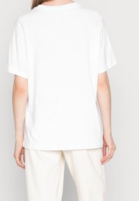 Vit kortärmad t-shirt sedd bakifrån, med avslappnad passform, rund halsringning och slät bomullstextur.