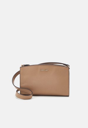 Mała beżowa skórzana torebka na ramię Calvin Klein z regulowanym paskiem i złotym logo z przodu.