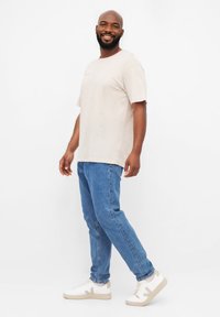 T-shirt en coton beige, coupe décontractée, manches courtes. Jean en denim bleu clair, coupe droite. Baskets blanches avec des accents gris et semelle texturée.