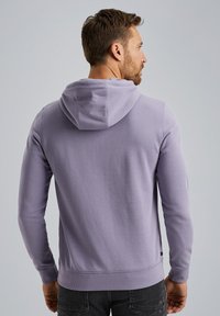 Lilac hoodie with a drawstring hood, ribbed cuffs, and hem. Features a smooth texture and a simple design, worn with dark jeans.