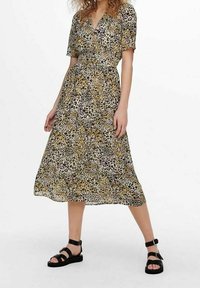 Robe midi à imprimé animal en beige et noir avec des manches courtes, un décolleté en V et une taille élastique. Portée avec des sandales noires à lanières.