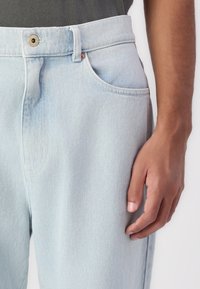 Light blue denim jeans with a high waist, a button closure, and side pockets. The fabric has a smooth texture and subtle grain pattern.