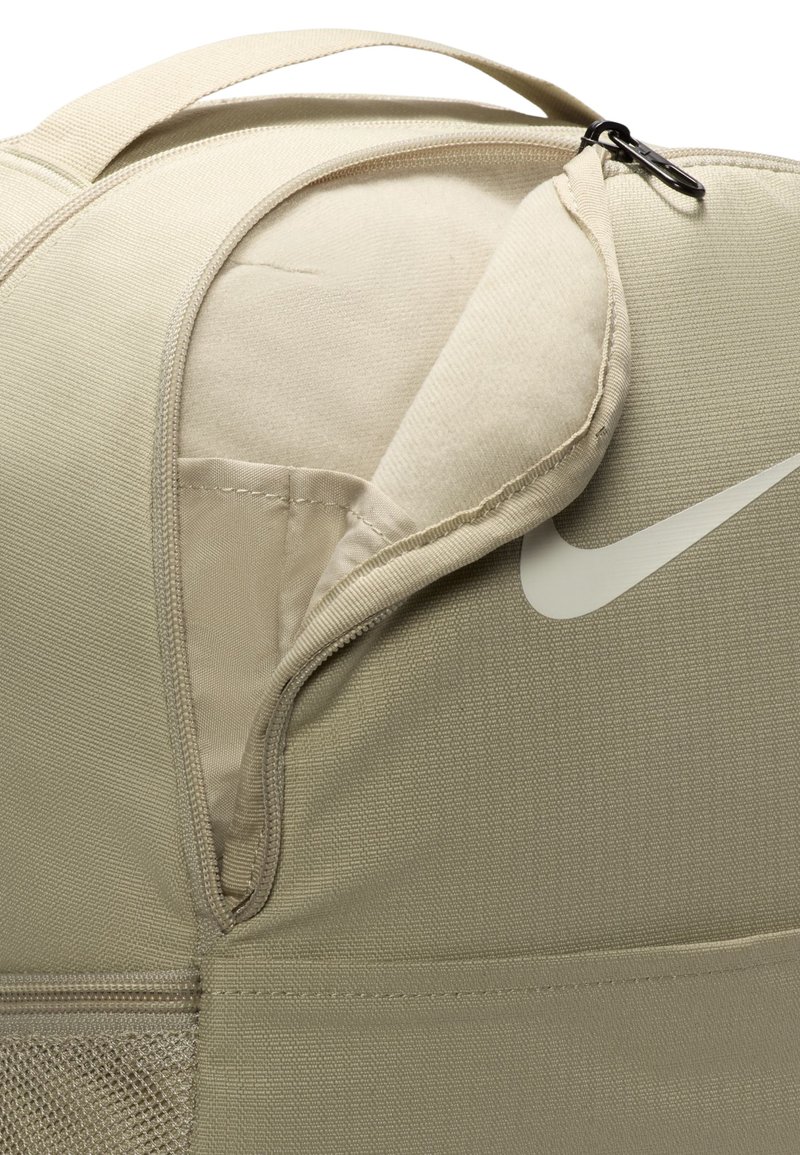 Beige nylon duffelväska med en zippered ficka, rund form, slät textur och en vit logotyp. Inkluderar ett robust handtag på toppen för bärande.