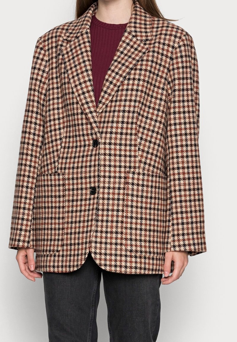 Veste à carreaux marron et beige en tissu texturé, dotée d'un col à revers cranté, d'une fermeture à un bouton et de deux poches avant.