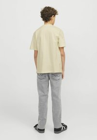 T-shirt di cotone giallo chiaro con maniche corte e scollatura rotonda, abbinato a jeans in denim grigio con cuciture a contrasto e tasche.