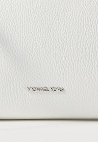 Hvidt lædermateriale med en tekstureret finish, der har en sølvmetallic "MICHAEL KORS"-logo præget på overfladen.