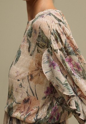 Kukkakuvioinen paita vaalean persikan värissä, jossa on teksturoitu, kiiltävä kangas. Ominaisuuksiin kuuluu rypytetyt hihat ja istuva vartalonosa.