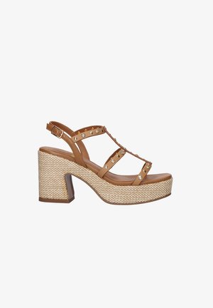 Sandalia de plataforma de cuero marrón con tacón grueso tejido, tira en T adornada con tachuelas doradas y plateadas, y hebilla ajustable en el tobillo.