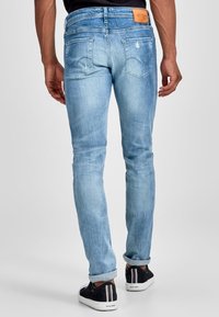 Light blue jeans with a slim fit, featuring a brown leather patch at the waist, distressed detailing on the back pockets, and rolled cuffs.