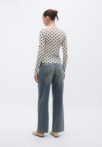 Off-white-värinen pitkähihainen pusero mustilla pilkkuilla, yhdistetty vaaleansinisiiin leveälahkeisiin farkkuihin. Rentoon asuun kuuluvat myös rennot kengät.