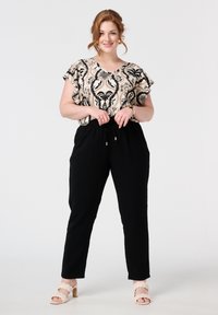 Zwarte tapering broek met een elastische tailleband, gecombineerd met een beige gemønsterd top met een v-hals en korte fladdermouwen.