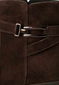 Bottines en daim marron avec une accent de boucle sur le côté et des détails en sangle. Présente une texture lisse et des coutures le long des seams.